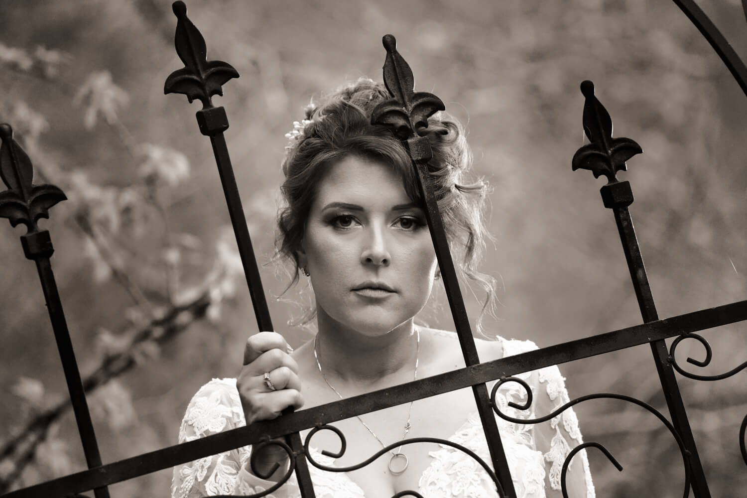 Black and white portrait of a bride standing behind an iron fence