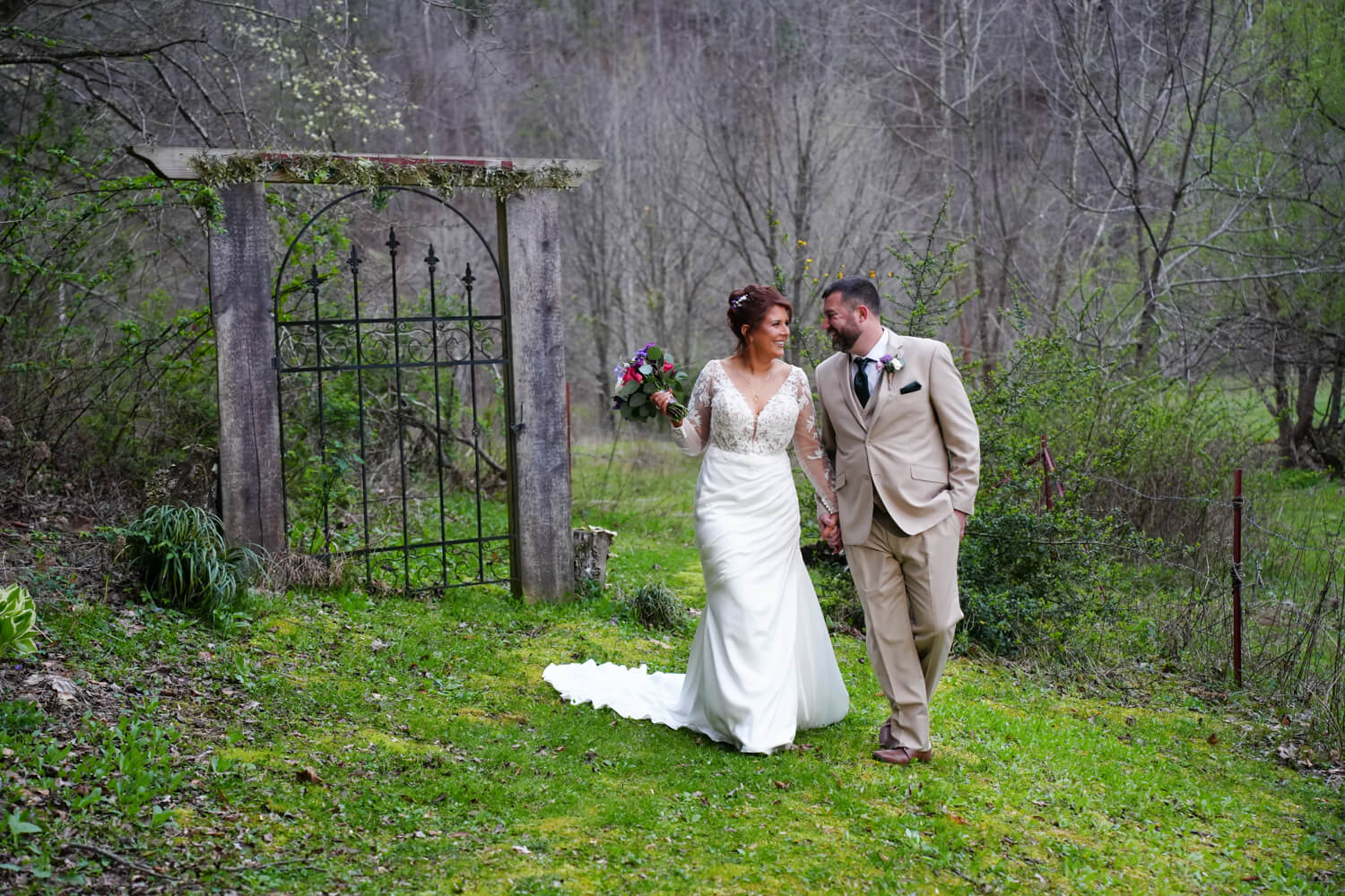Bride and groom walking together and laughing near an iron gate in the woods