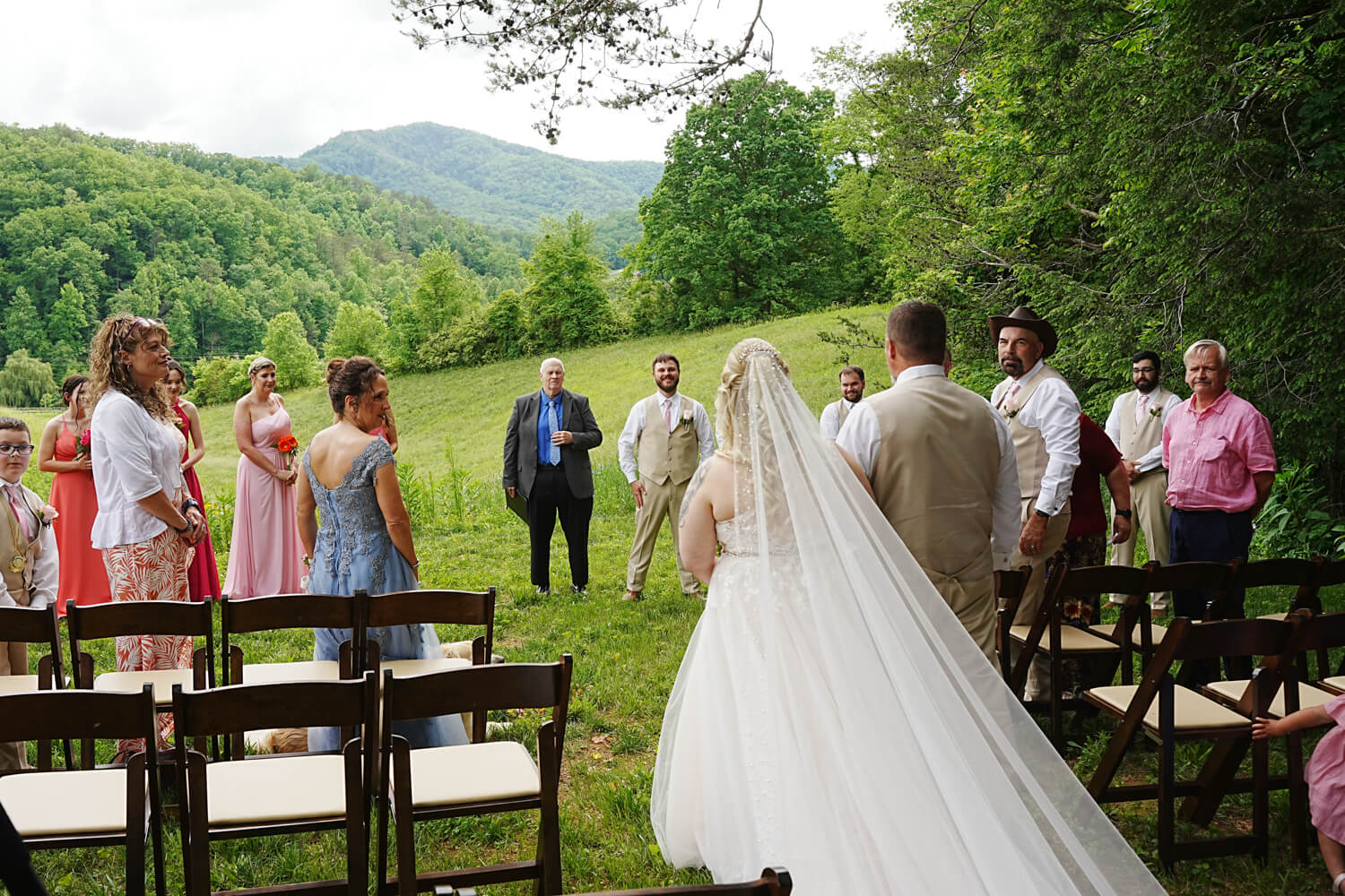 Bride escorted by her father down the aisle at a mountain view ceremony site in a field