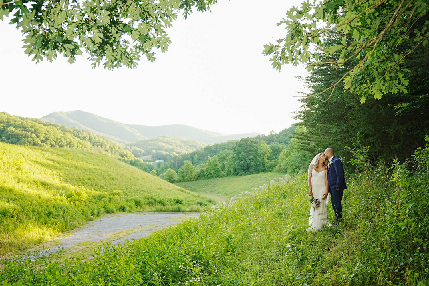 Wedding Couple at a mountain view in a field with summer trees framing the scene