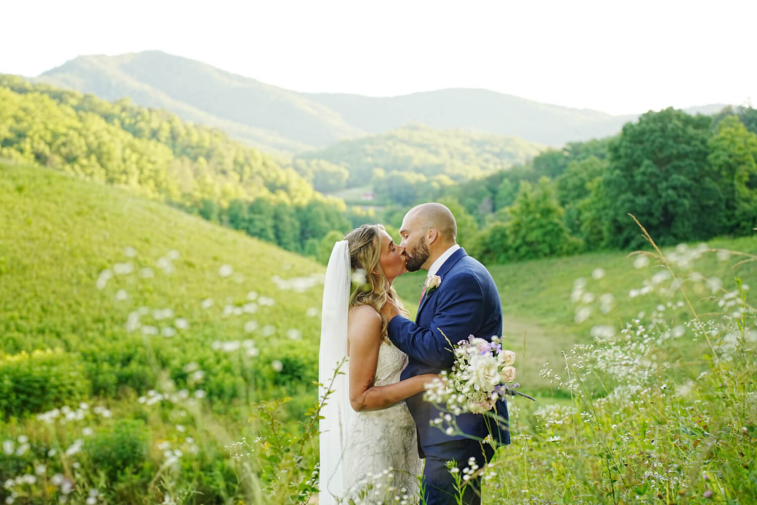 Weddign couple kissing in front of white daisies at a mountain view