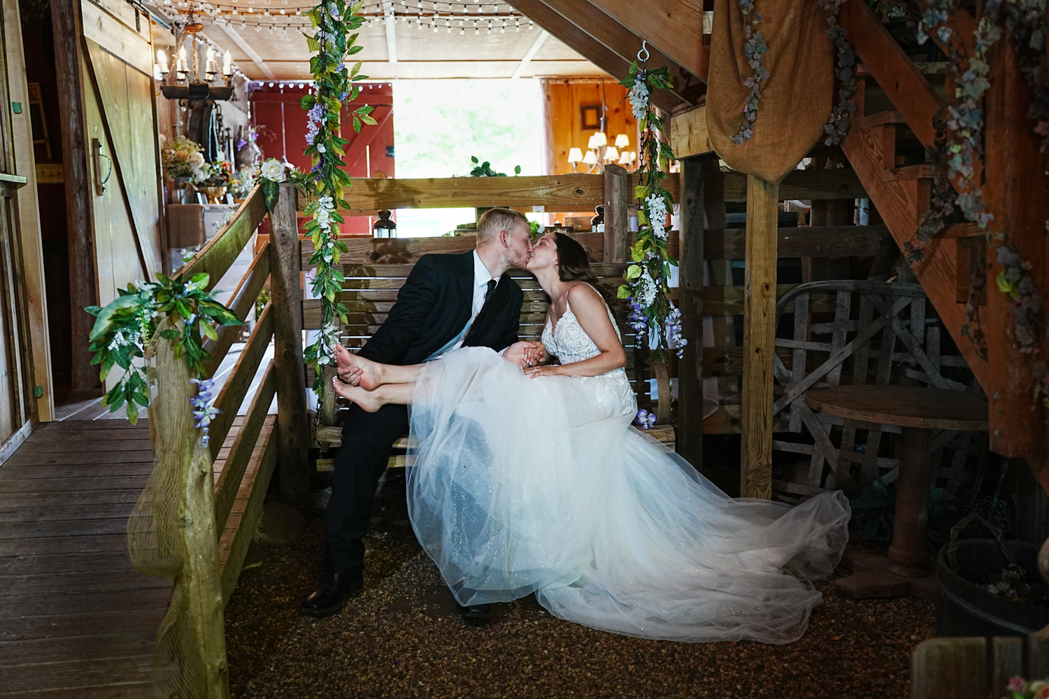barefoot bride kissing her groom in a porch swing in a barn wedding venue in Pigeon Forge