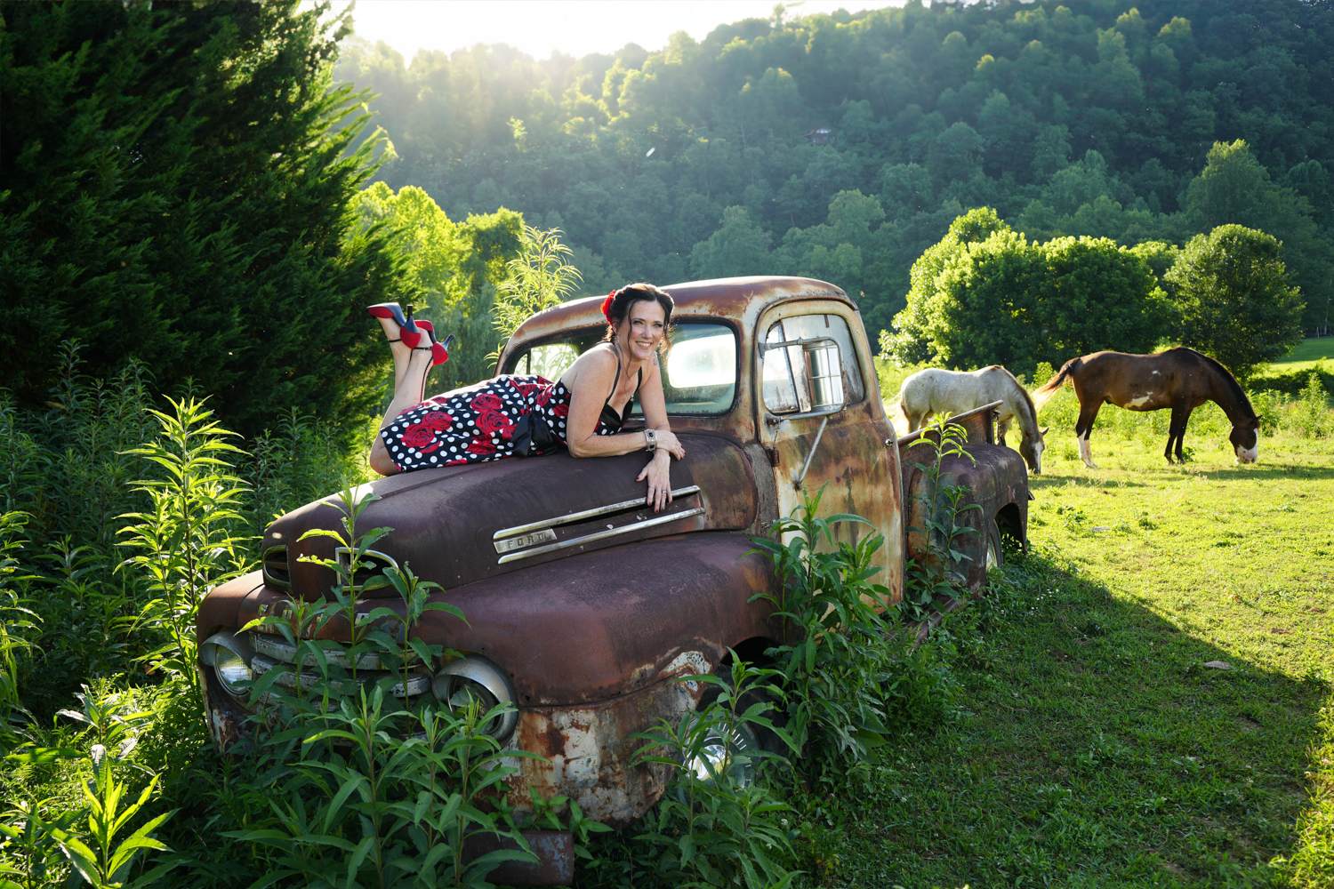Rockabilly style portrait of a woman in a pin up dress laying on the hood of an old 1950 Ford truck