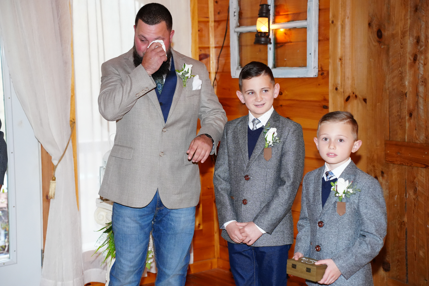 Groom wiping a tear from his eye in a wedding chapel standing next to his smiling sons