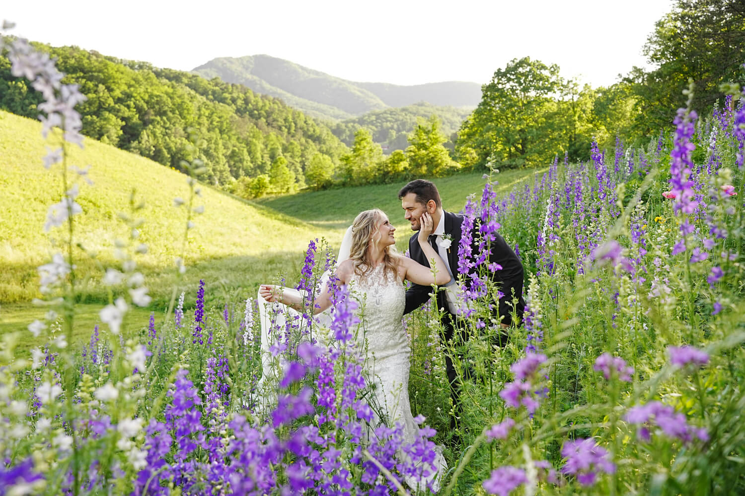 wedding couple in a field of purple larkspur with rolling hills and a mountain ridge behind them