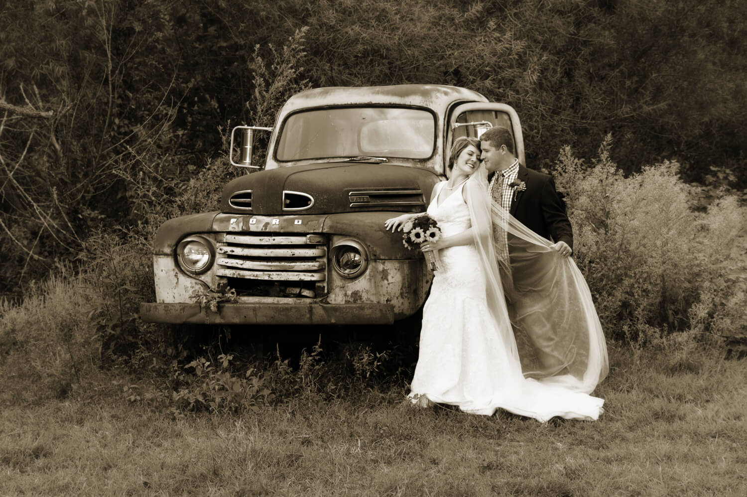 Bride with long veil kissing her groom in front of a 1950 Ford truck on their wedding day in Pigeon Forge