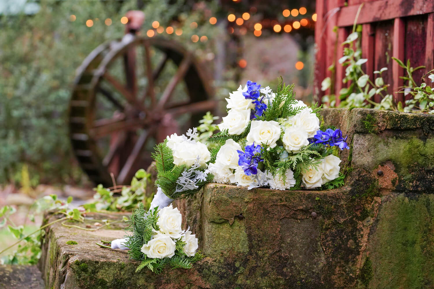 Wedding bouquet with white and blue flowers sitting on stone steps in front of a water wheel
