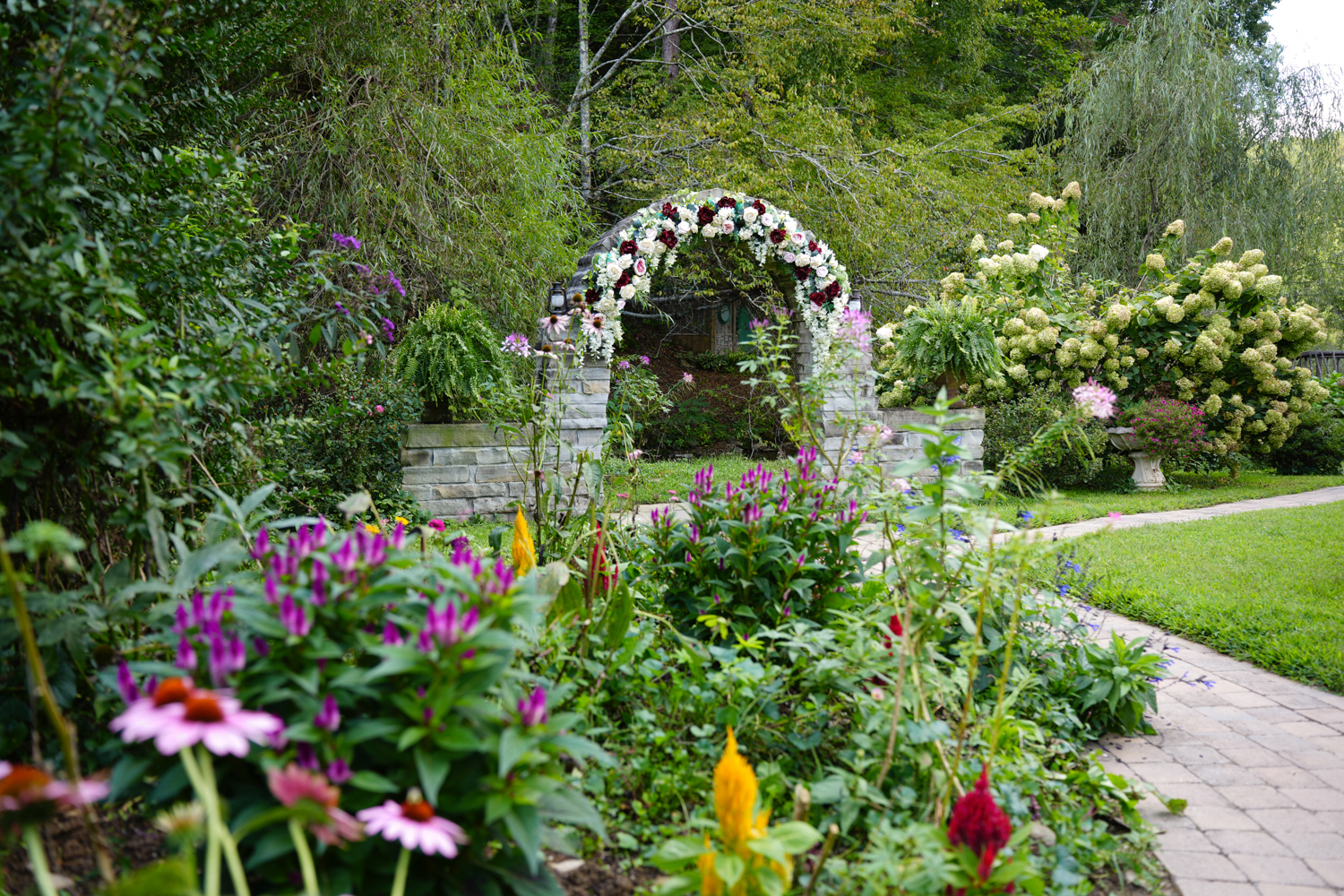 Stone archway decorated with white and navy blue flowers in front of a fall wildflower garden