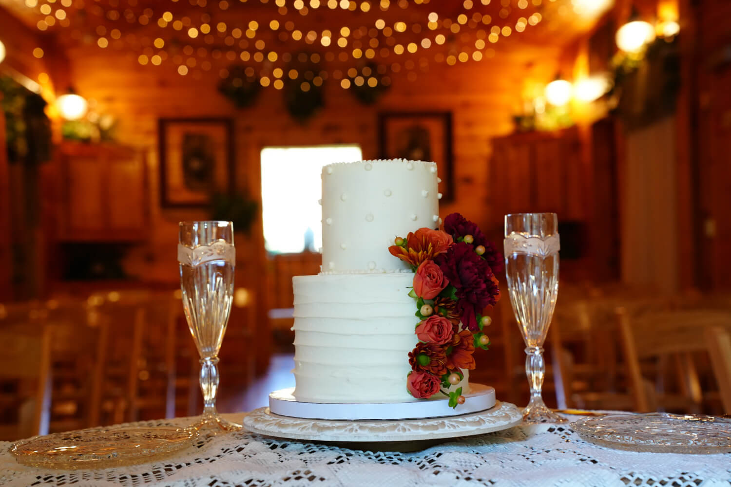 Wedding cake and toasting glasses sitting on a table in a wedding chapel with pine wood walls and twinkling lights hanging from the ceiling