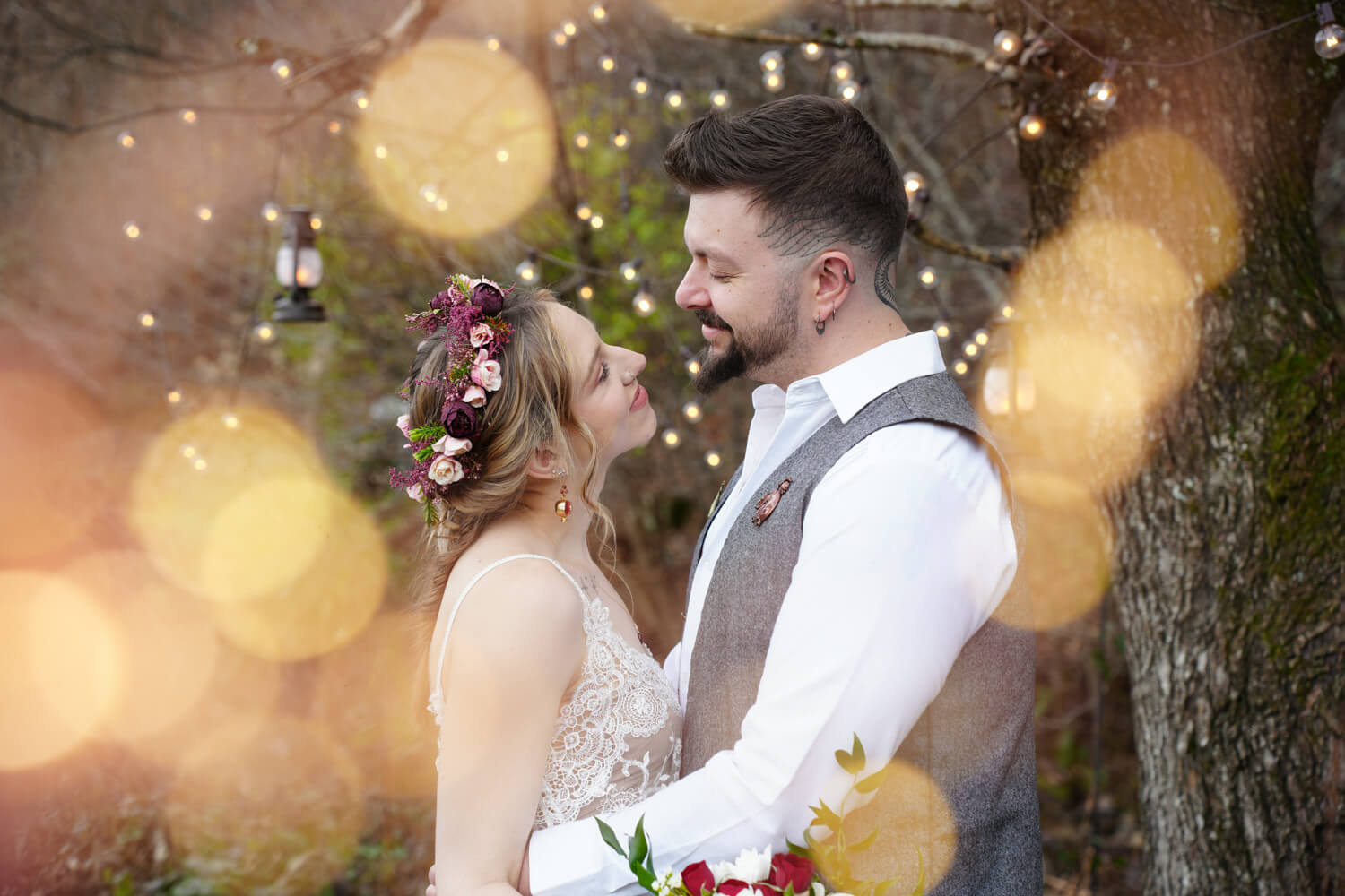 Boho style bride and groom under twinkling lights of a willow tree in the fall