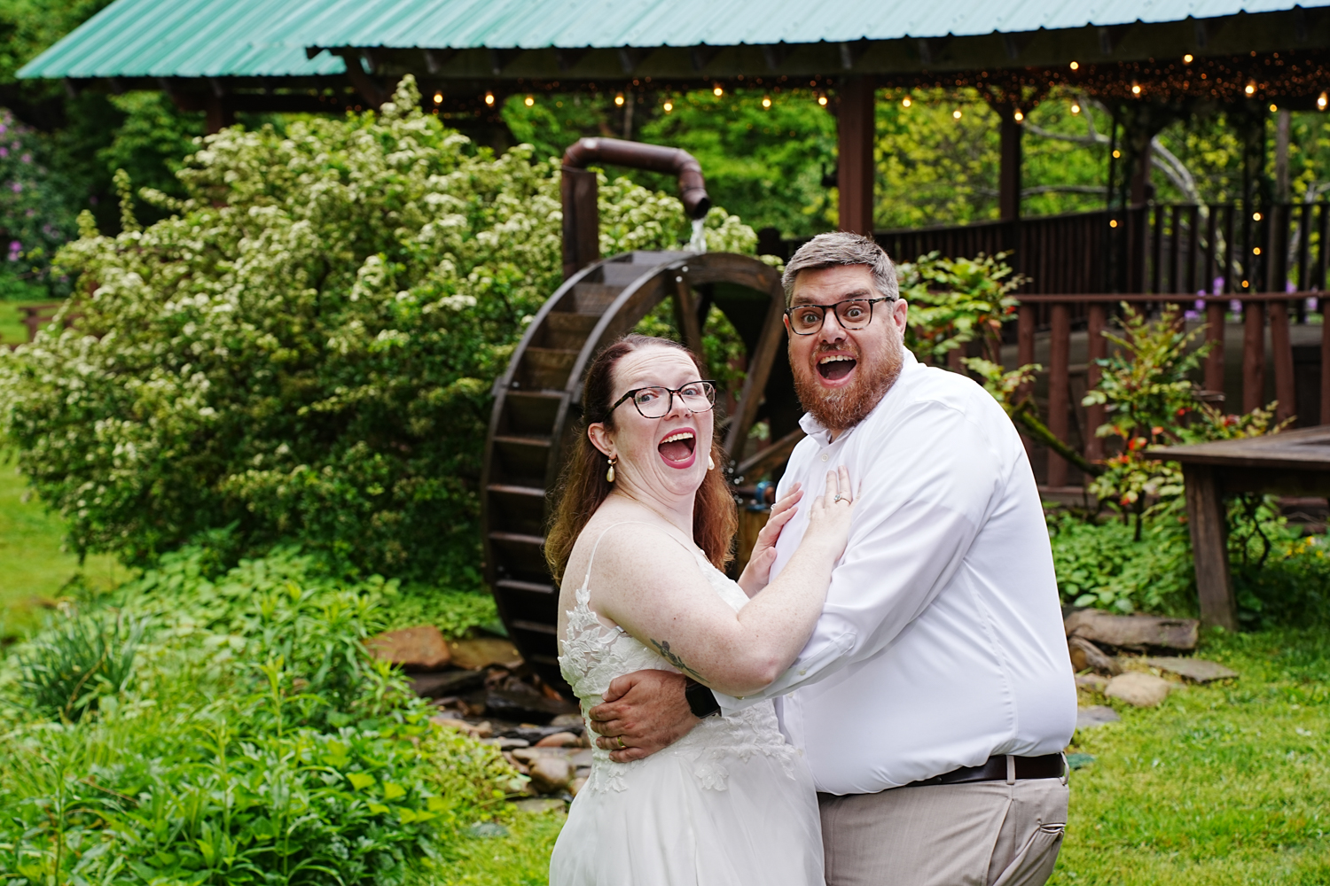 Wedding couple laughing with their mouths wide open in front of a water wheel at their wedding venue in Pigeon Forge