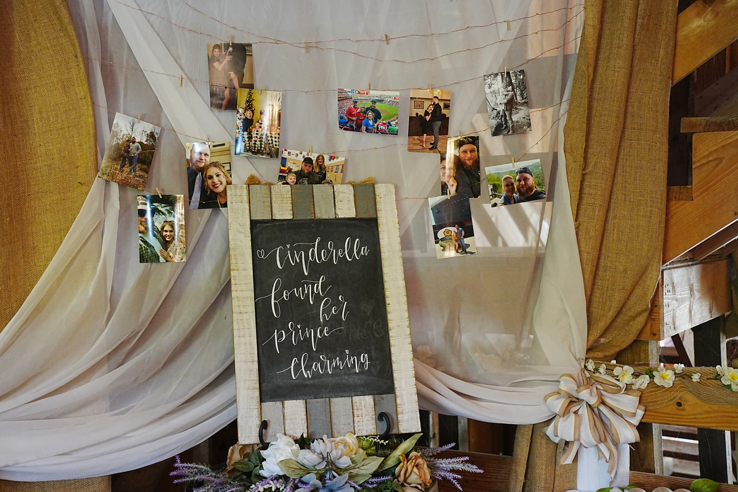 Pictures hung on clothes pins in an entry way to a barn wedding venue with a cinderella met her prince charming sign