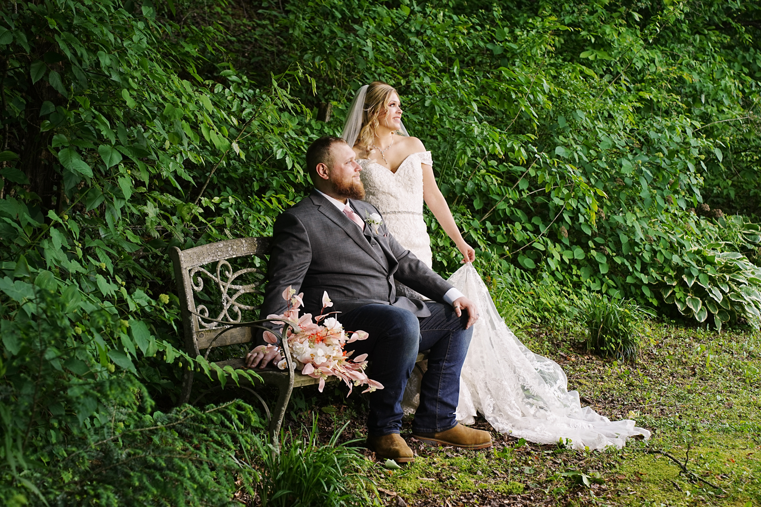 Bride and groom sitting on a park bench in a forest in the summer on their wedding day