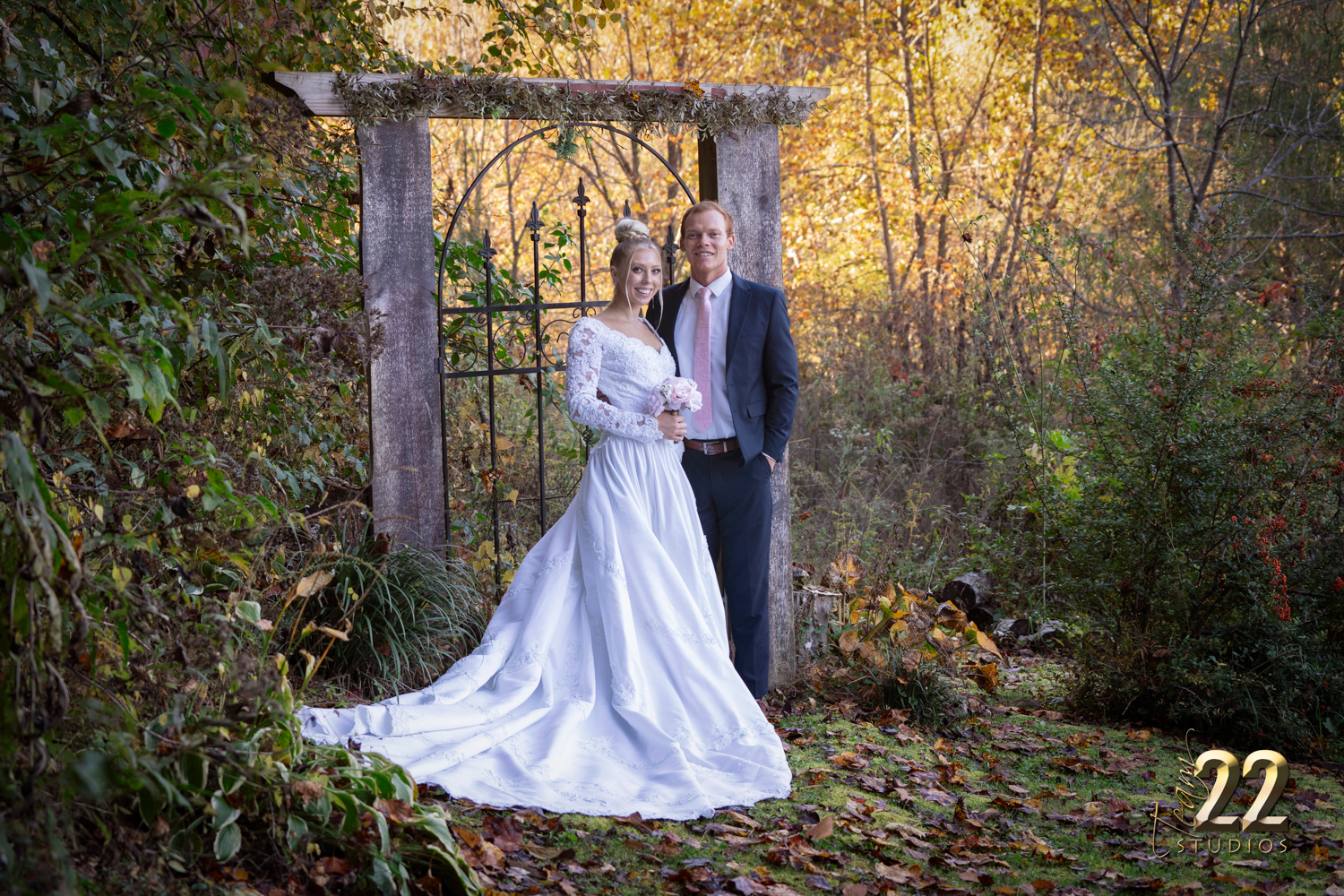 Bride and groom posing at a black iron gate in the fall