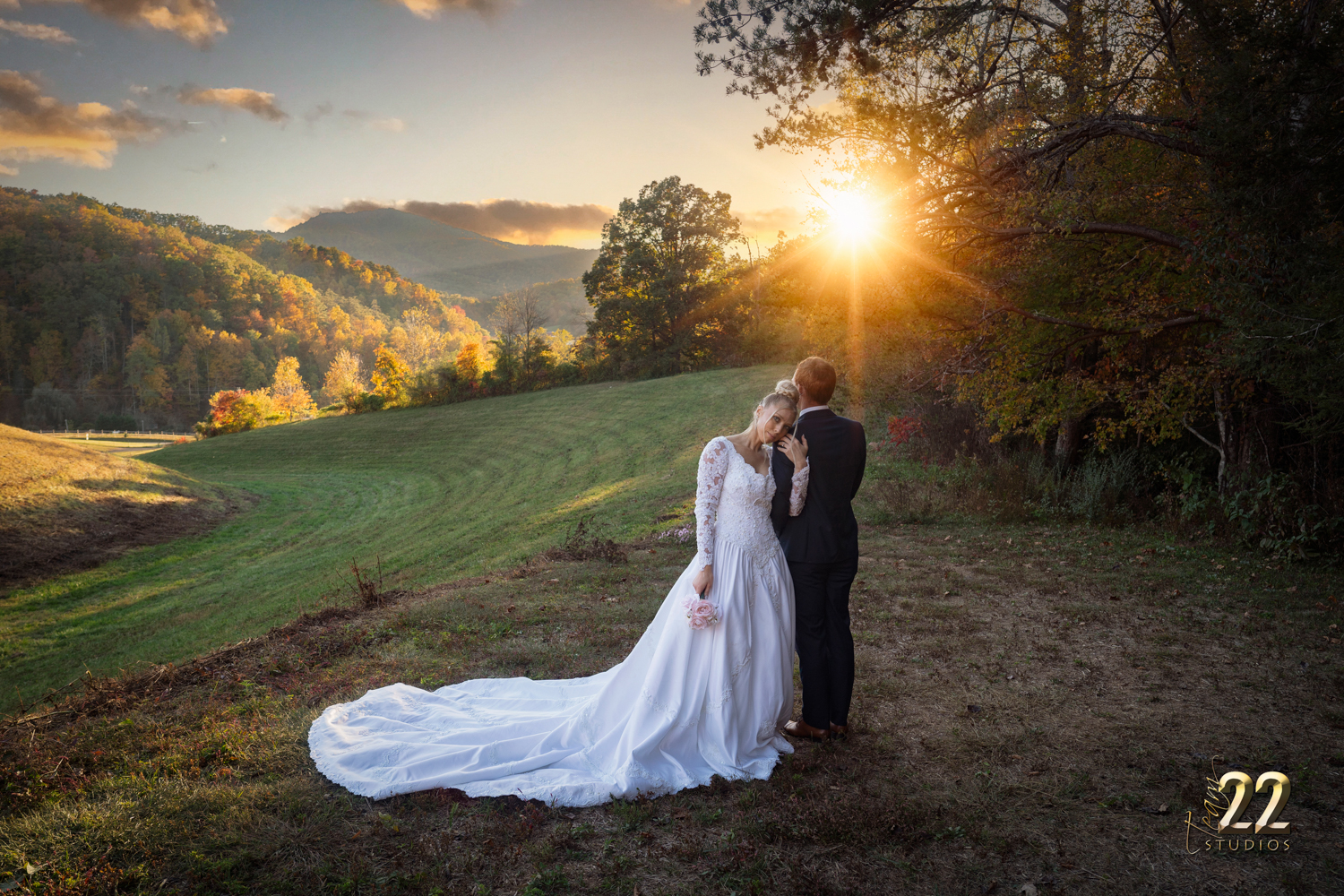 Bride leaning on her groom's shoulder as the sun sets in a meadow