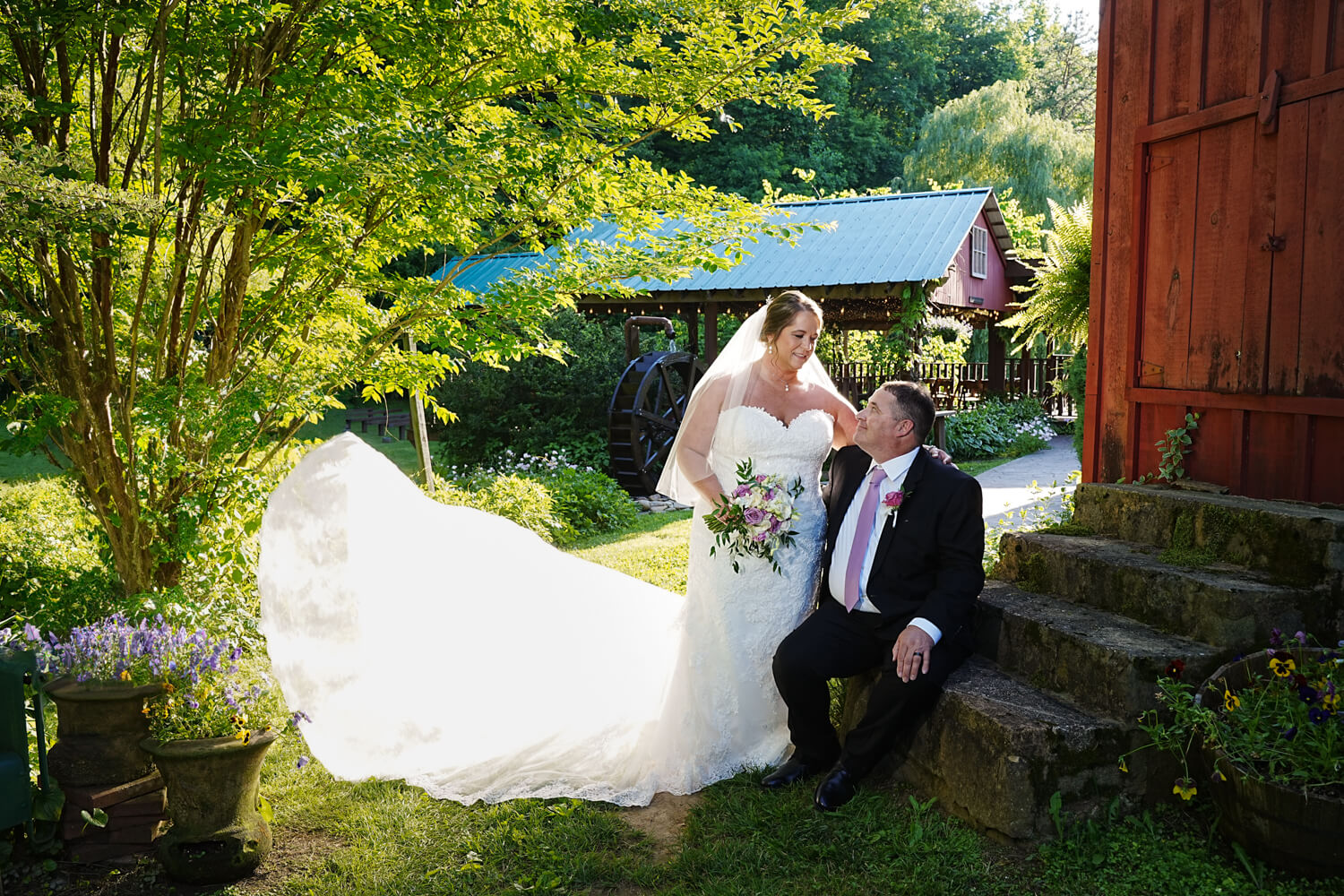 bride's train blowing in the wind behind her as she touches her husband gently at a barn wedding venue in Pigeon Forge