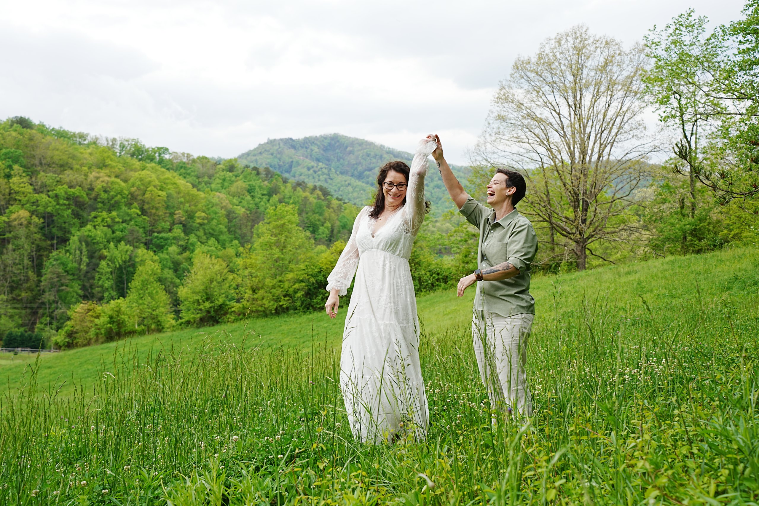 Same sex female wedding couple dancing in a field at a mountain view on their wedding day