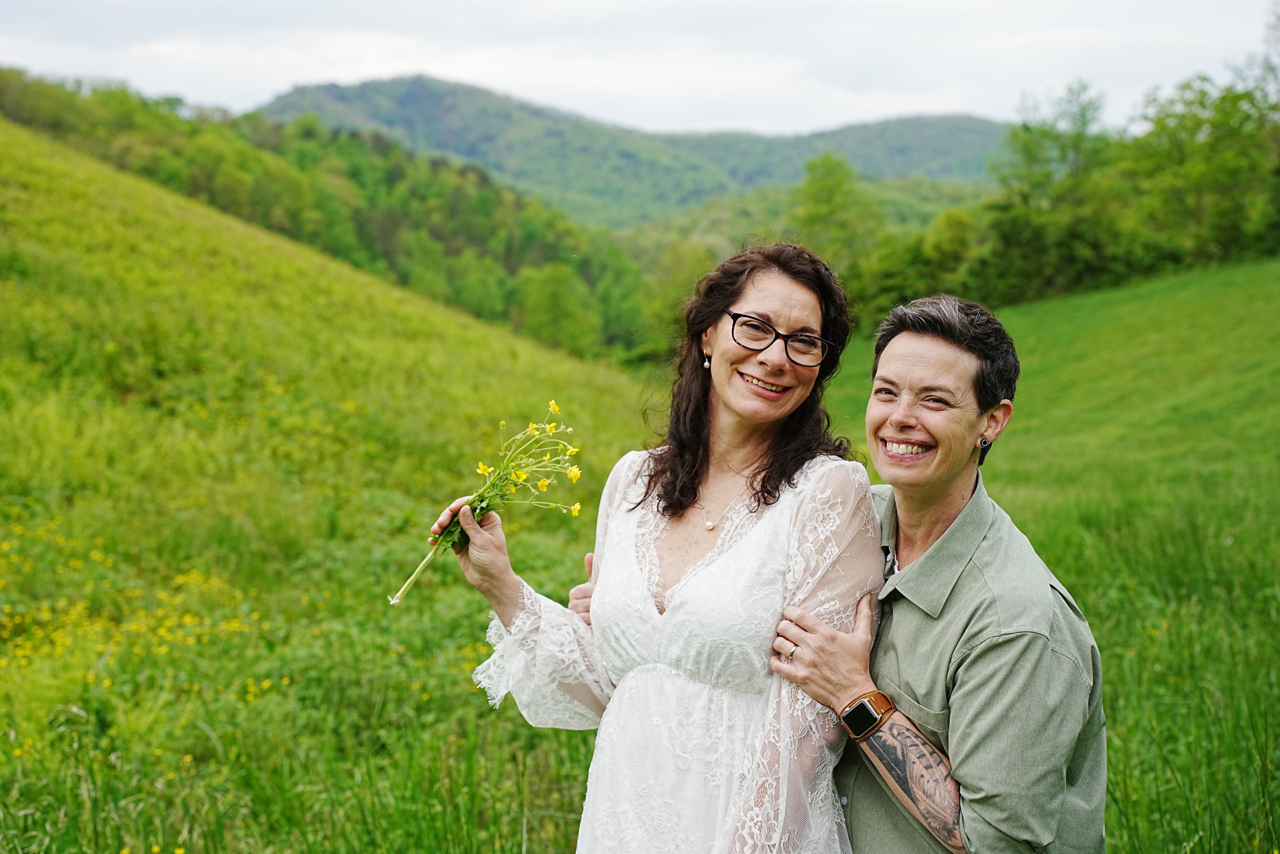 Bride and bride at a mountain view in the spring holding yellow flowers