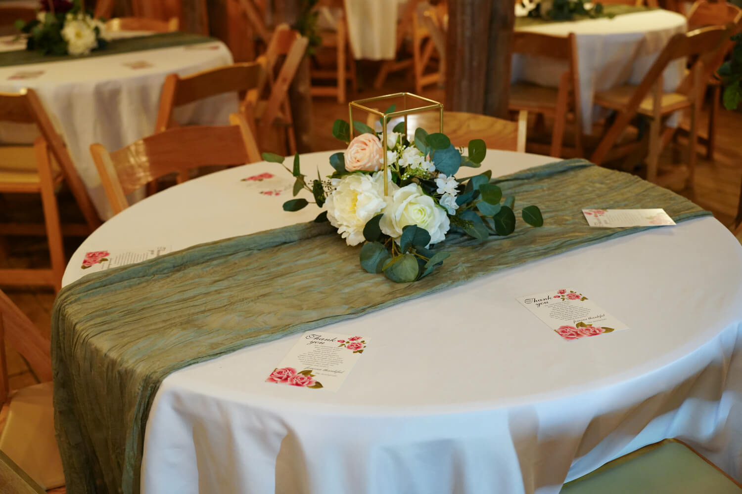 Table with white cloth and crepe sage runner with a centerpiece of flowers in the middle for a wedding reception