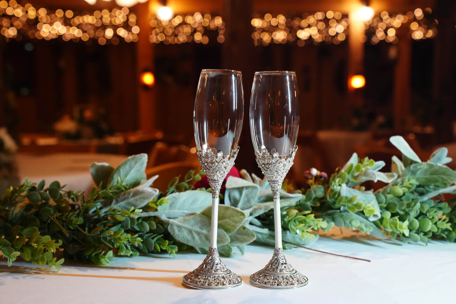 two champagne glasses sitting on a white table cloth with warm fairy lights behind them in a reception area