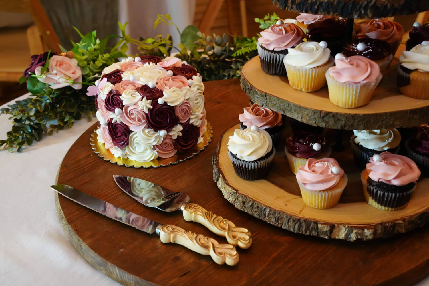 small weddign cake sitting next to a cupcake stand made from tree trunks in a wedding reception hall