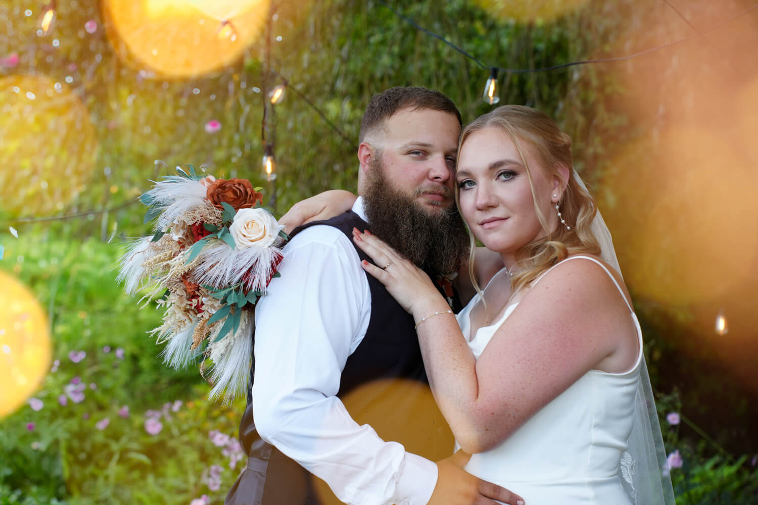 Bride and Groom holding each other under a willow tree with golden bokeh lights all around them and fairy lights in the background