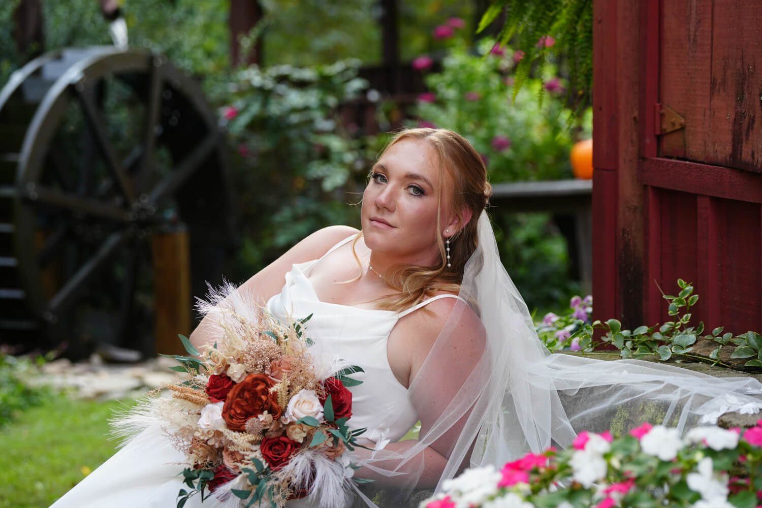 Bride leaning back on a set of steps by a water wheel at a country wedding venue called Honeysuckle Hills