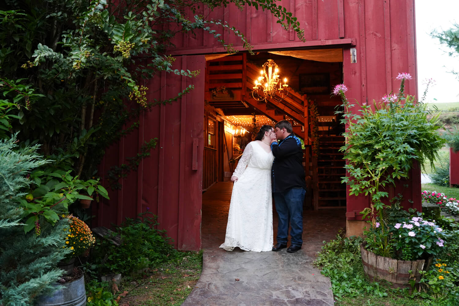 couple kissing in a red barn with a rustic chandelier hanging above them with golden light