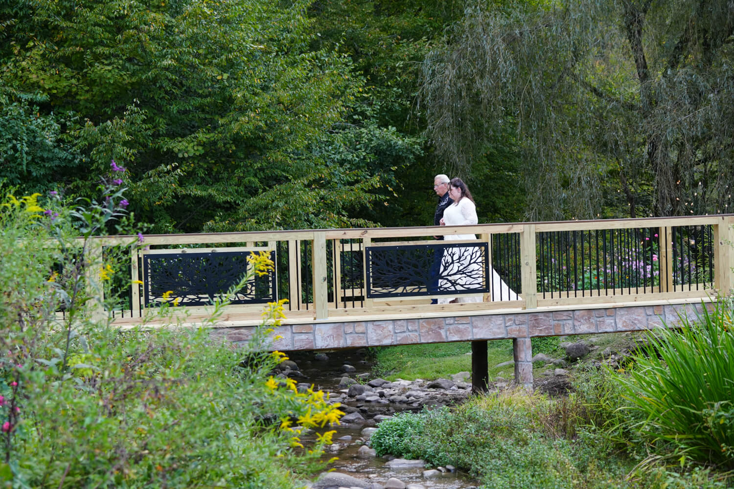 Grandfather walking bride down the aisle across a long wooden bridge with iron and stone decor