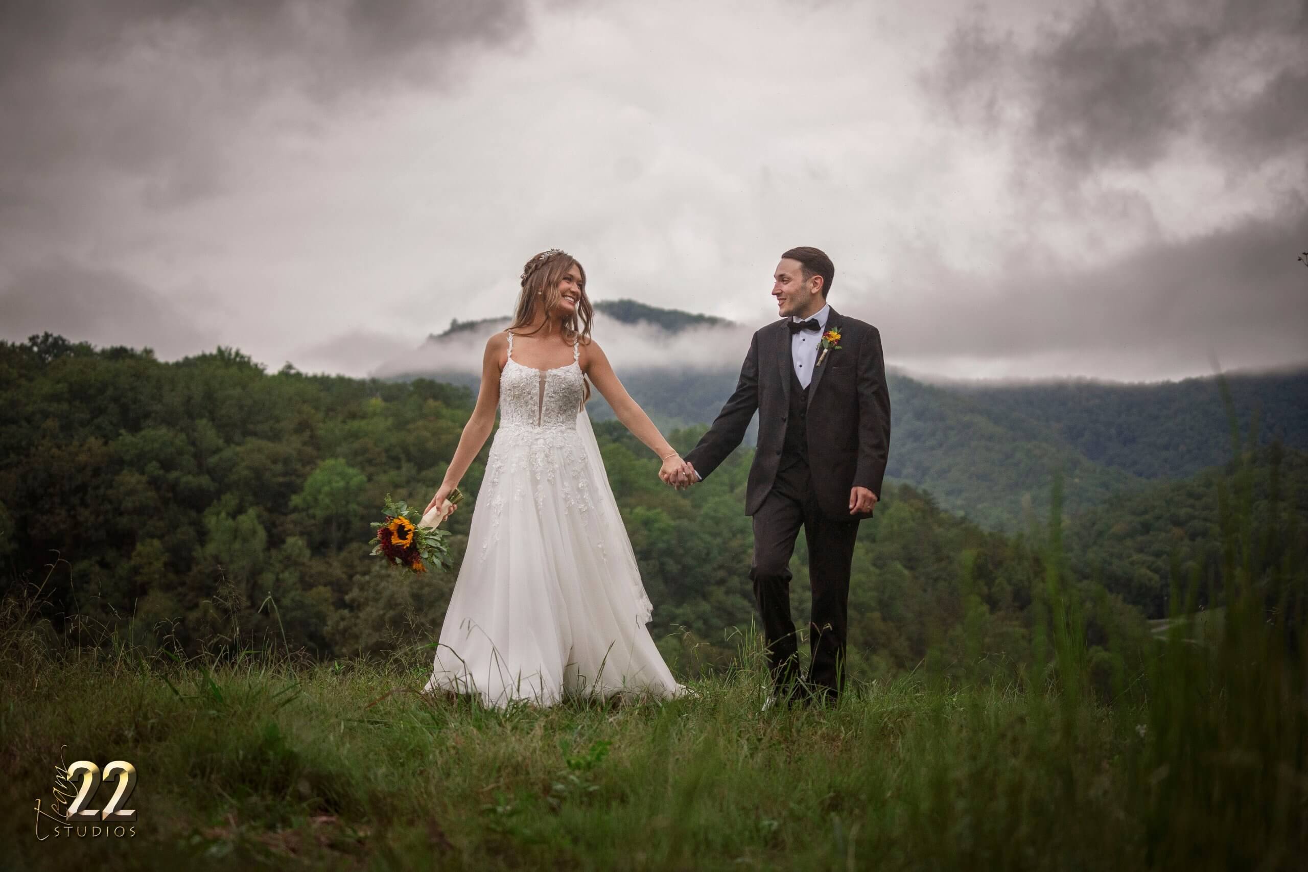 Bride and groom walking in a field with fog in the background exposing the tip of a mountain