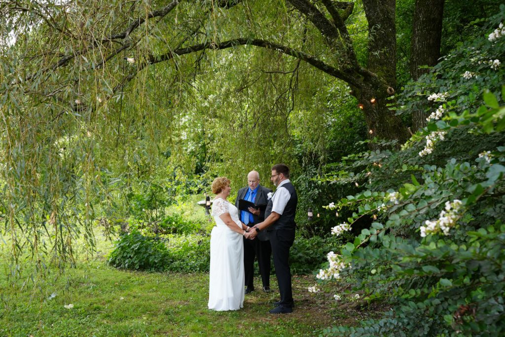 Couple getting married under a willow tree with white crepe myrtles blooming next to it