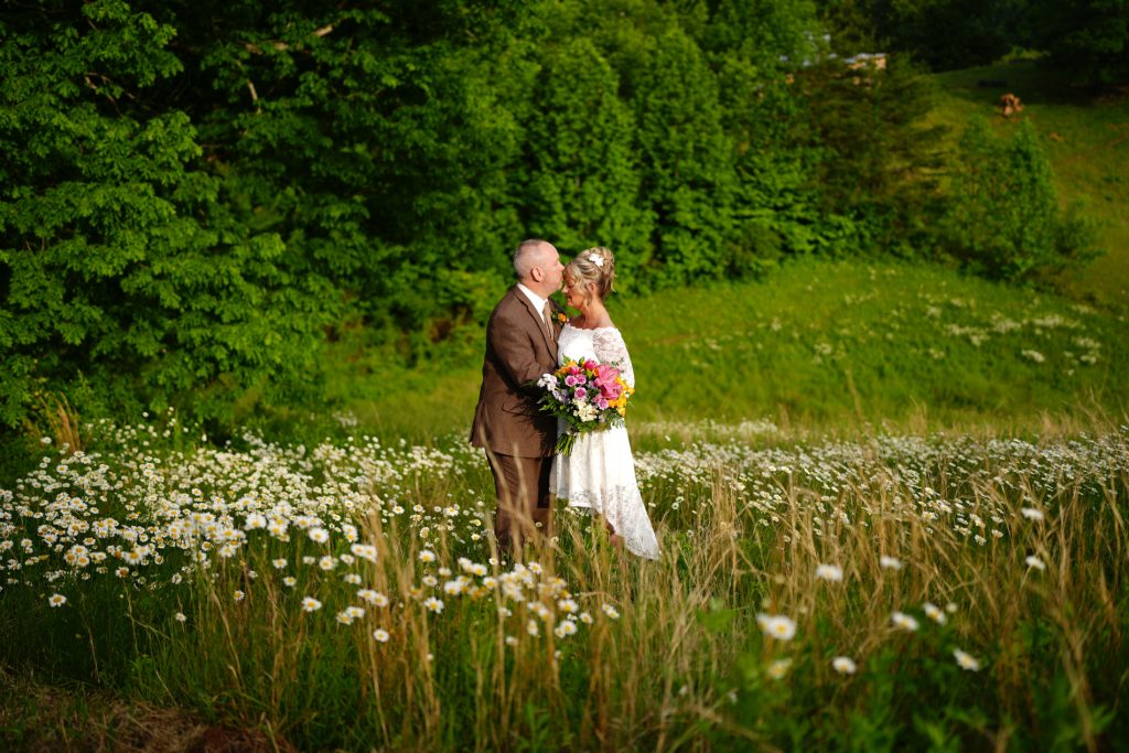 Groom kissing his bride's forehead in a field of daisies at the mountain adventure site at Honeysuckle Hills in Pigeon Forge