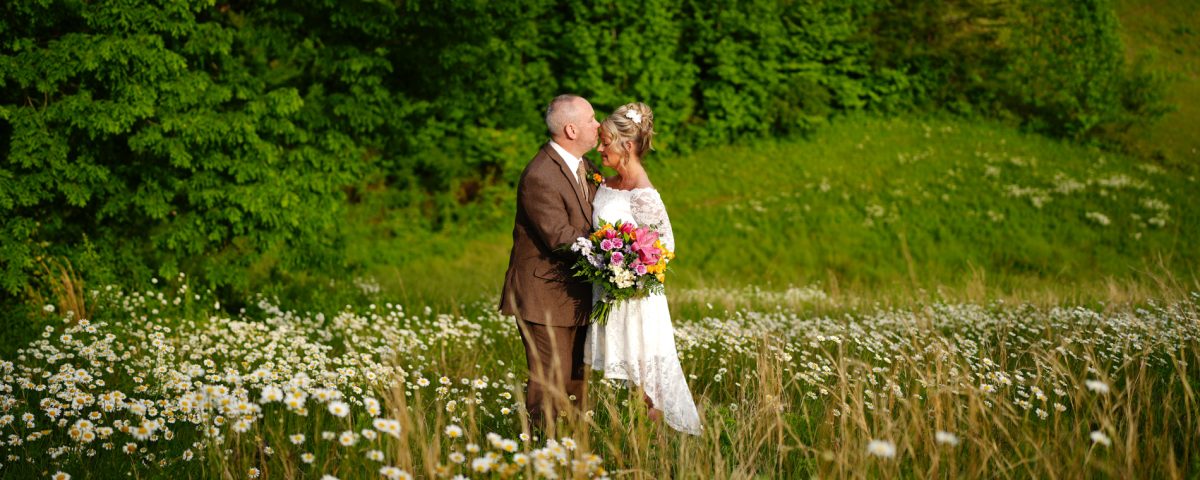 Groom kissing his bride's forehead in a field of daisies at the mountain adventure site at Honeysuckle Hills in Pigeon Forge