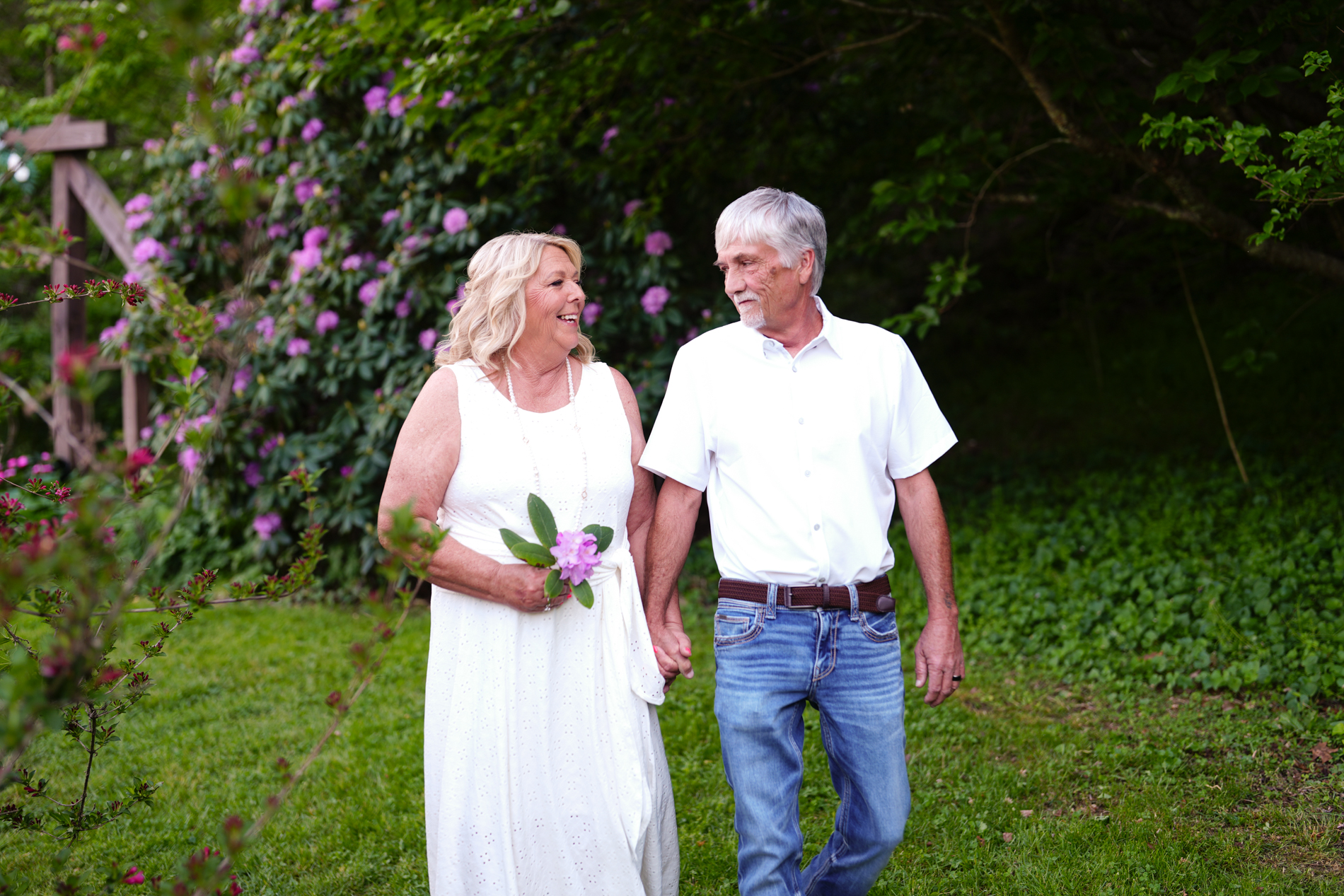 Golden years couple walking in the wedding gardens at Honeysuckle Hills in the spring by the rhododendrons after their elopement ceremony